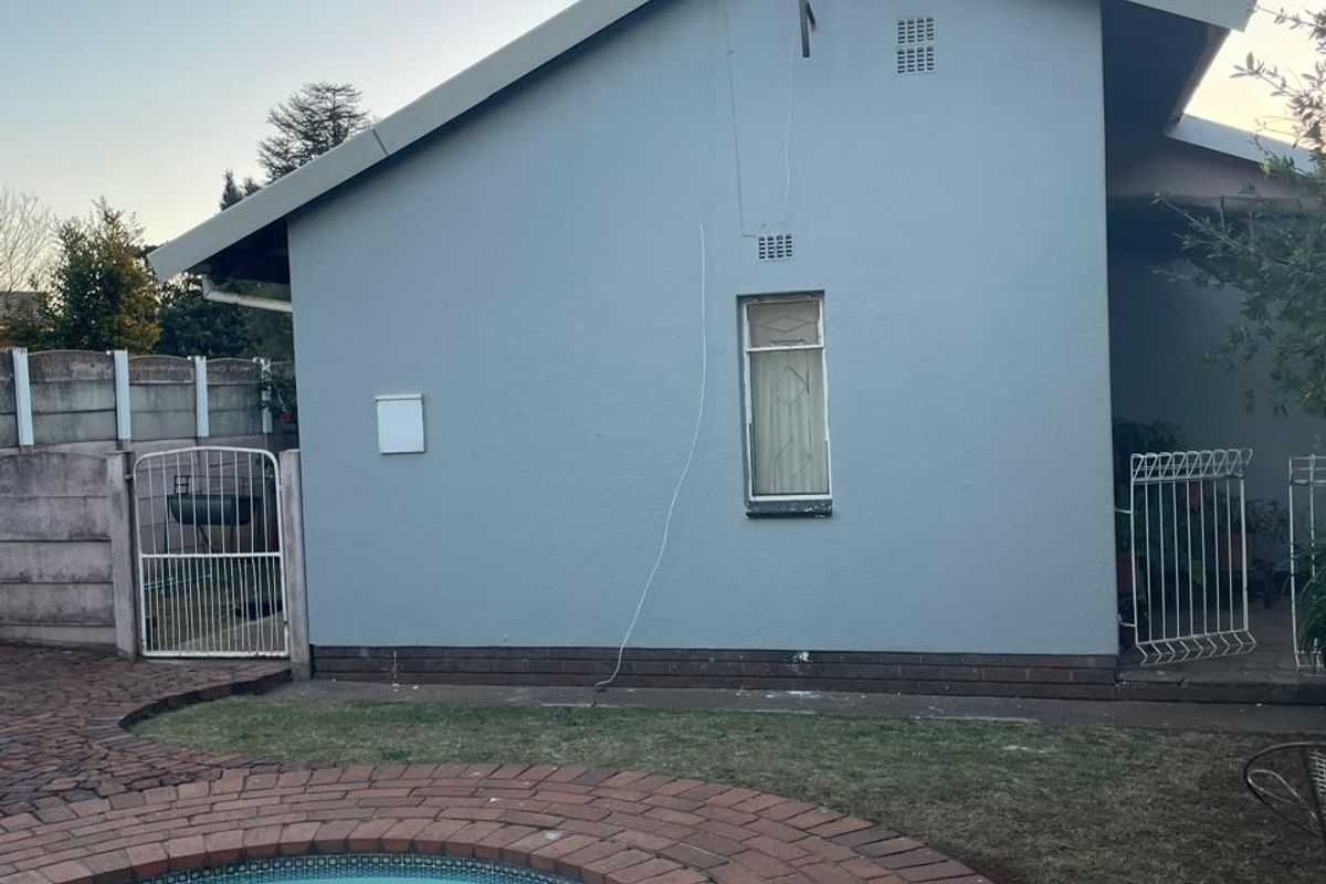 Rear exterior view of the house featuring a swimming pool with brick paving, a precast boundary wall, and a metal security gate.