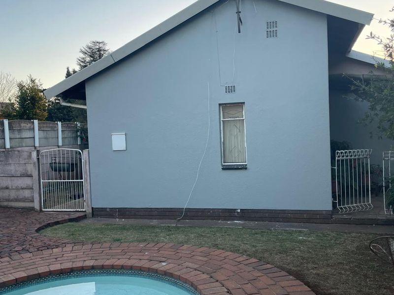 Rear exterior view of the house featuring a swimming pool with brick paving, a precast boundary wall, and a metal security gate.