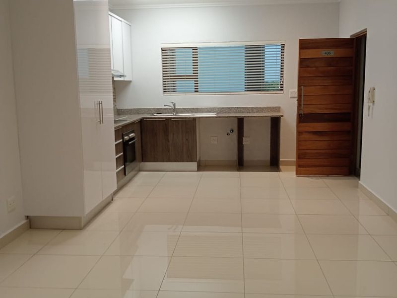 Modern open-plan kitchen and living area featuring sleek cabinetry, granite countertops, tiled flooring, and recessed lighting in a clean, vacant space.