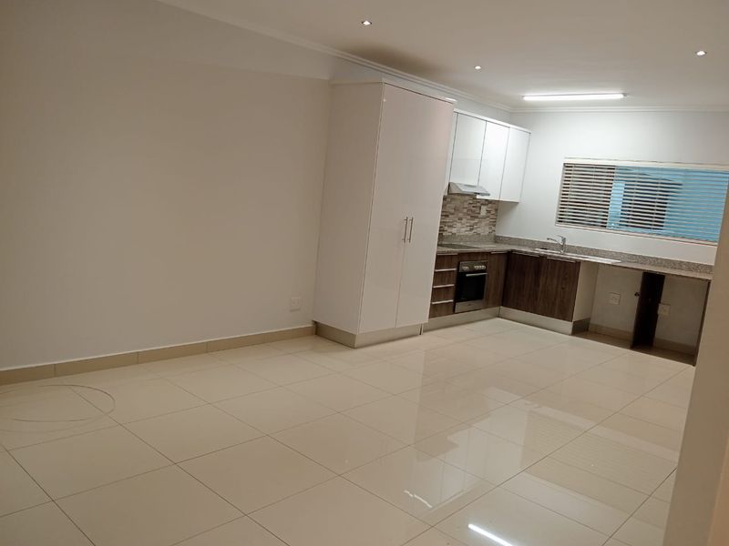 A modern open-plan kitchen featuring sleek cabinetry, stone countertops, built-in appliances, and polished tiled flooring in a bright, well-maintained space.