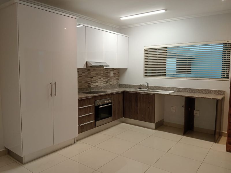 Modern kitchen featuring white and wood-grain cabinetry, stone-look countertops, built-in oven, hob, extractor fan, and tiled flooring with a neutral mosaic backsplash.