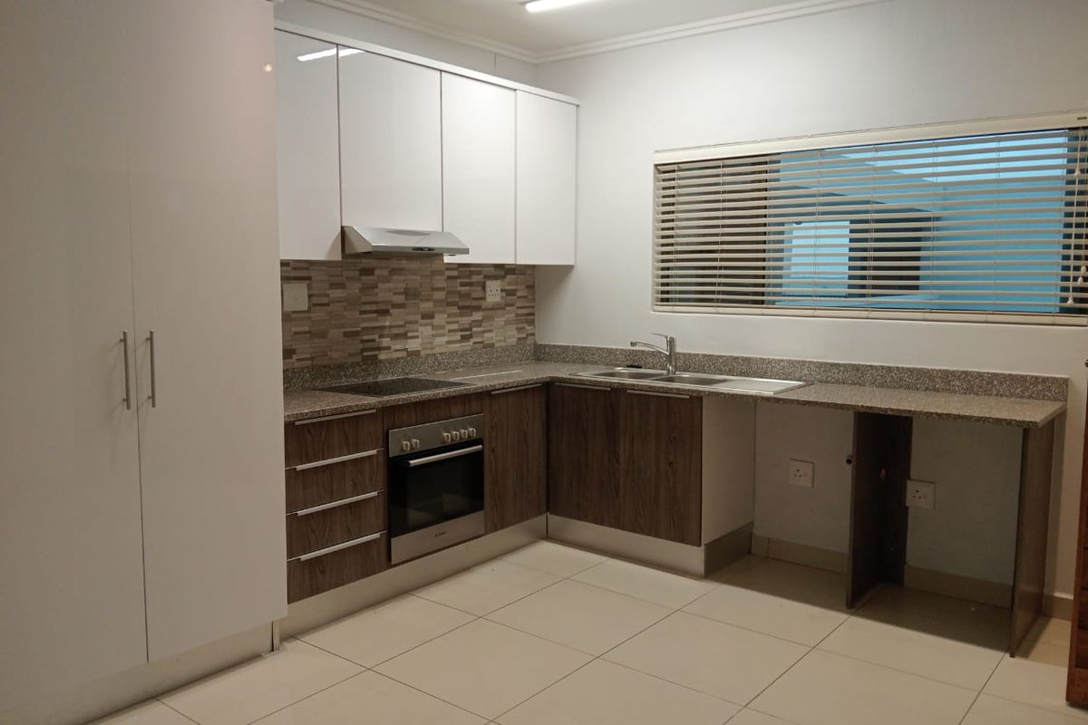 Modern kitchen featuring white and wood-grain cabinetry, stone countertops, built-in oven, electric hob, and tiled flooring with ample storage space.