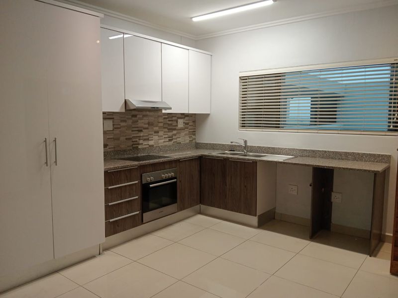 Modern kitchen featuring white and wood-grain cabinetry, stone countertops, built-in oven, electric hob, and tiled flooring with ample storage space.