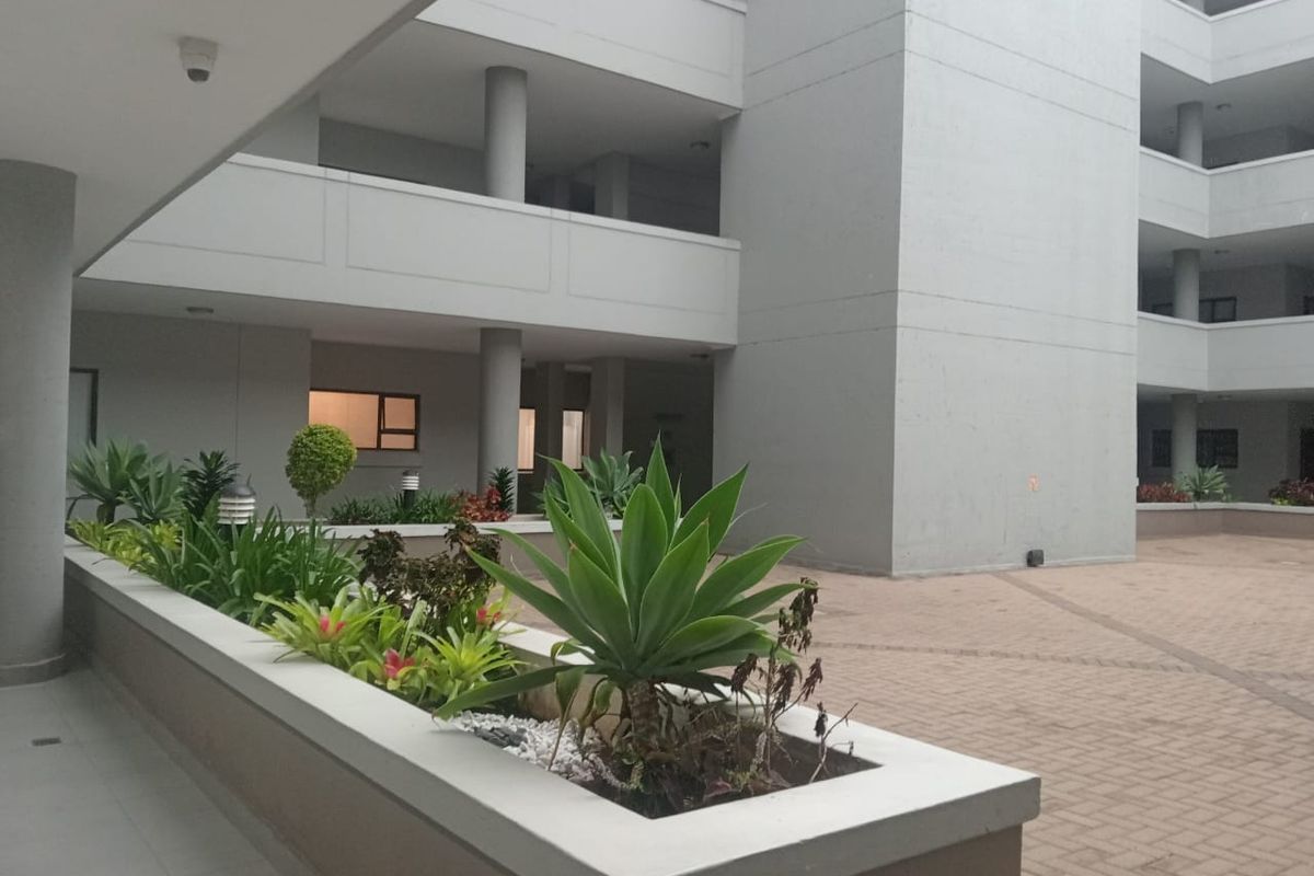 A well-maintained apartment complex courtyard featuring paved walkways, structural concrete columns, and a raised planter bed with established landscaping.