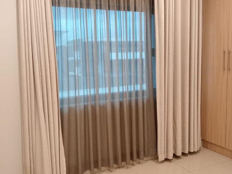 A bright, empty bedroom featuring neutral tiled flooring and a large built-in wardrobe with modern finishes.