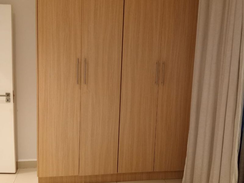 A clean bedroom interior featuring light wood-finish built-in wardrobes and neutral tiled flooring.