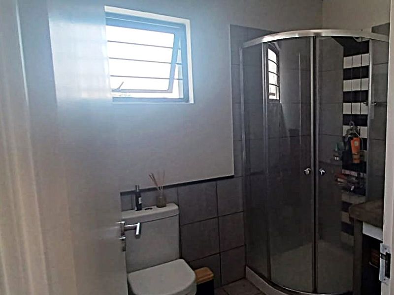 A functional bathroom featuring a corner shower enclosure, a standard toilet, and tiled finishes throughout.