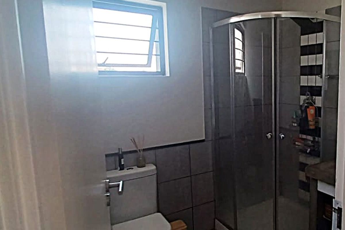 A functional bathroom featuring a corner shower enclosure, a standard toilet, and tiled finishes throughout.