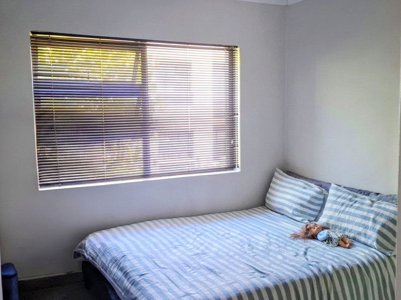 A simple bedroom featuring neutral walls, carpeted flooring, and a window fitted with venetian blinds.