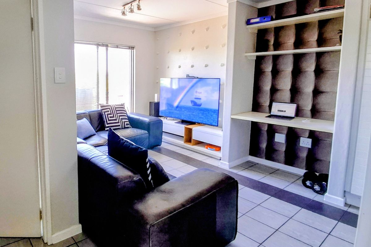 A living room featuring tiled flooring, built-in shelving, and a dedicated desk area, providing a functional space for relaxation and work.