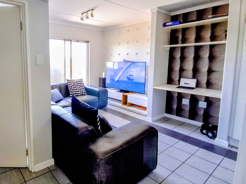 A living room featuring tiled flooring, built-in shelving, and a dedicated desk area, providing a functional space for relaxation and work.