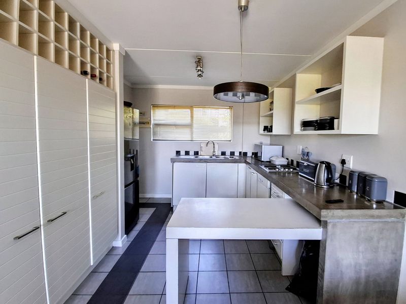 Modern kitchen featuring concrete countertops, ample built-in cabinetry with integrated wine storage, tiled flooring, and functional open shelving.