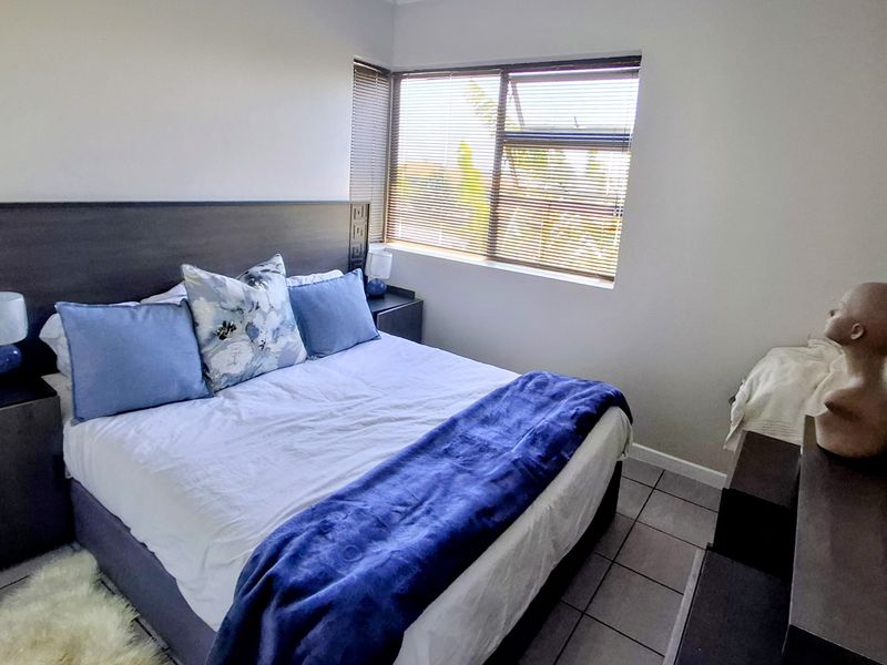 A functional bedroom featuring tiled flooring and fitted venetian blinds, offering a neutral space ready for personalization.