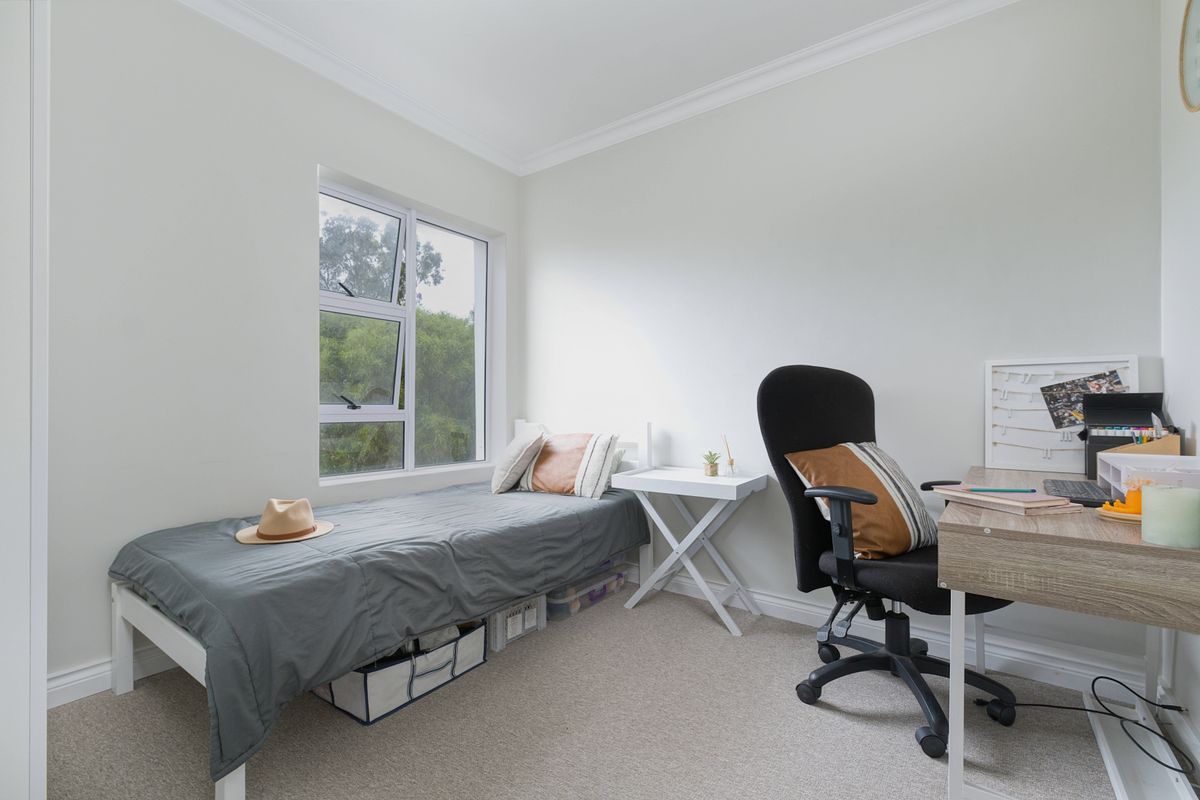 A well-maintained bedroom featuring neutral wall tones, carpeted flooring, and a large casement window providing natural light and garden views.