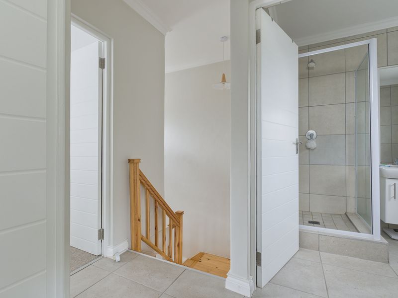 A bright hallway featuring a wooden staircase and access to a modern bathroom with a tiled shower enclosure and vanity basin.