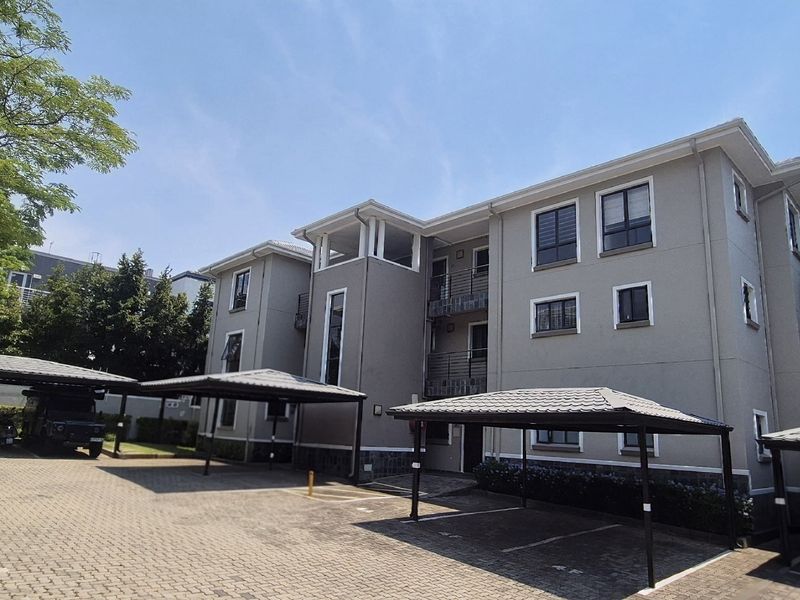 Exterior view of a multi-story apartment complex featuring a paved parking area with multiple covered carports and well-maintained building facades.