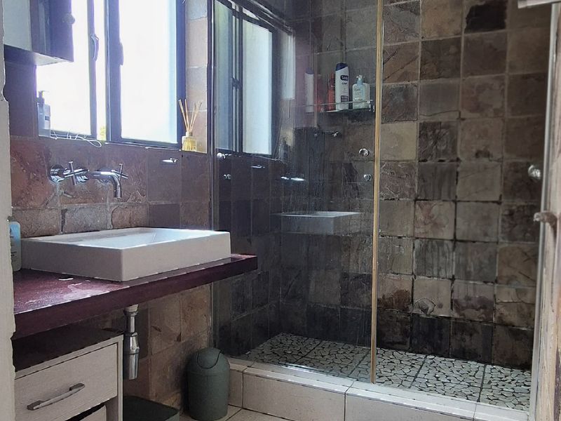 A functional bathroom featuring a walk-in shower with glass enclosure, stone wall tiling, and a modern vessel sink with wall-mounted faucet.