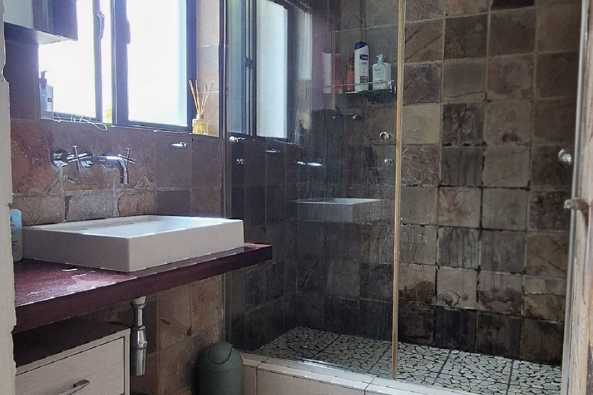 A functional bathroom featuring a walk-in shower with glass enclosure, stone wall tiling, and a modern vessel sink with wall-mounted faucet.