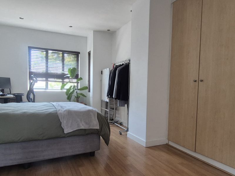 Spacious bedroom featuring light wood-finish built-in cupboards, laminate flooring, and recessed downlighting, offering a clean and functional living space.