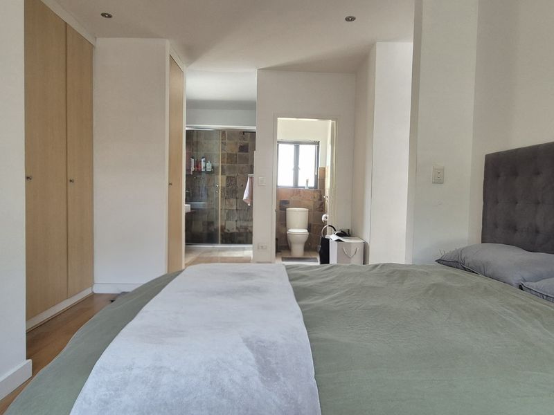 A well-maintained bedroom featuring built-in cupboards, recessed lighting, and an adjoining en-suite bathroom with a shower and toilet.
