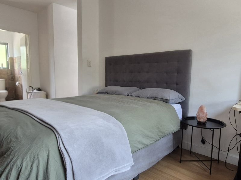 A bedroom featuring laminate flooring and an adjoining en-suite bathroom with a glass-enclosed shower and tiled finishes.