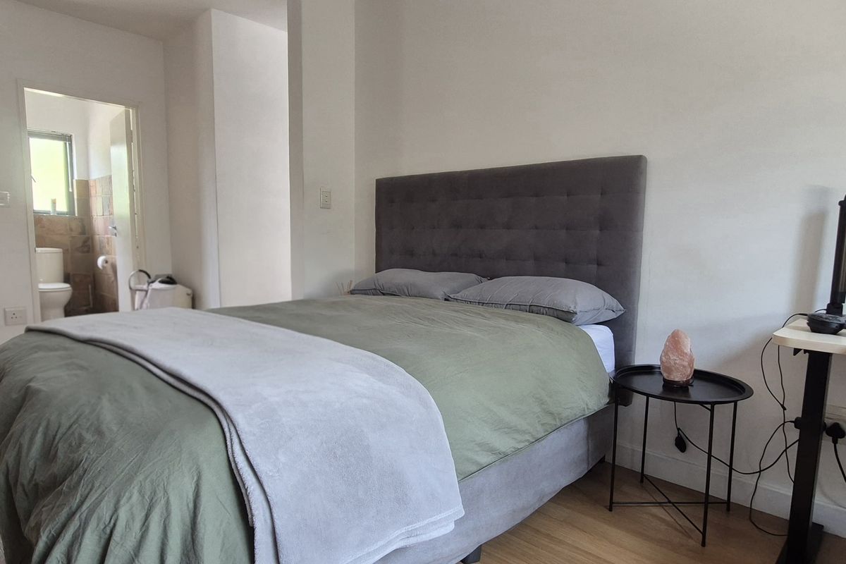 A bedroom featuring laminate flooring and an adjoining en-suite bathroom with a glass-enclosed shower and tiled finishes.