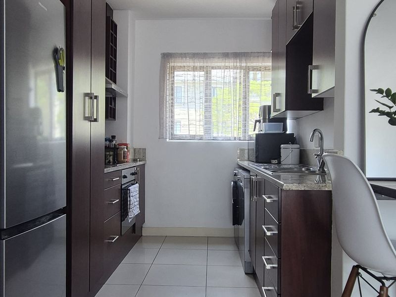 A galley-style kitchen featuring dark wood cabinetry, granite countertops, stainless steel sink, built-in oven, and polished tiled flooring.