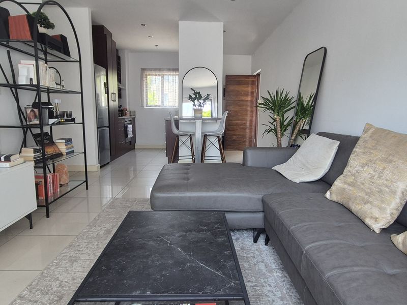 A modern open-plan living and kitchen area featuring sleek tiled flooring, recessed lighting, and contemporary cabinetry, creating a bright and functional living space.