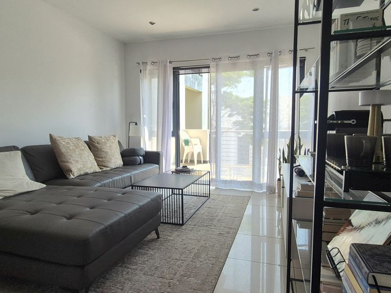 A bright living room featuring tiled flooring and a large sliding glass door providing access to an outdoor balcony area.