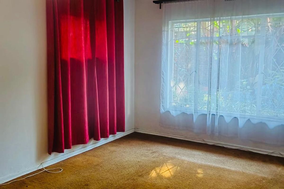 An empty bedroom featuring carpet flooring, a ceiling fan, and large windows with security bars, offering a blank canvas for renovation.