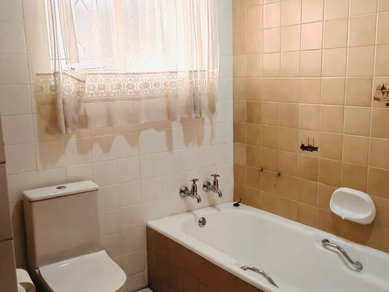 A functional bathroom featuring a bathtub, toilet, and tiled finishes. The space is well-maintained but features dated decor and tiling.