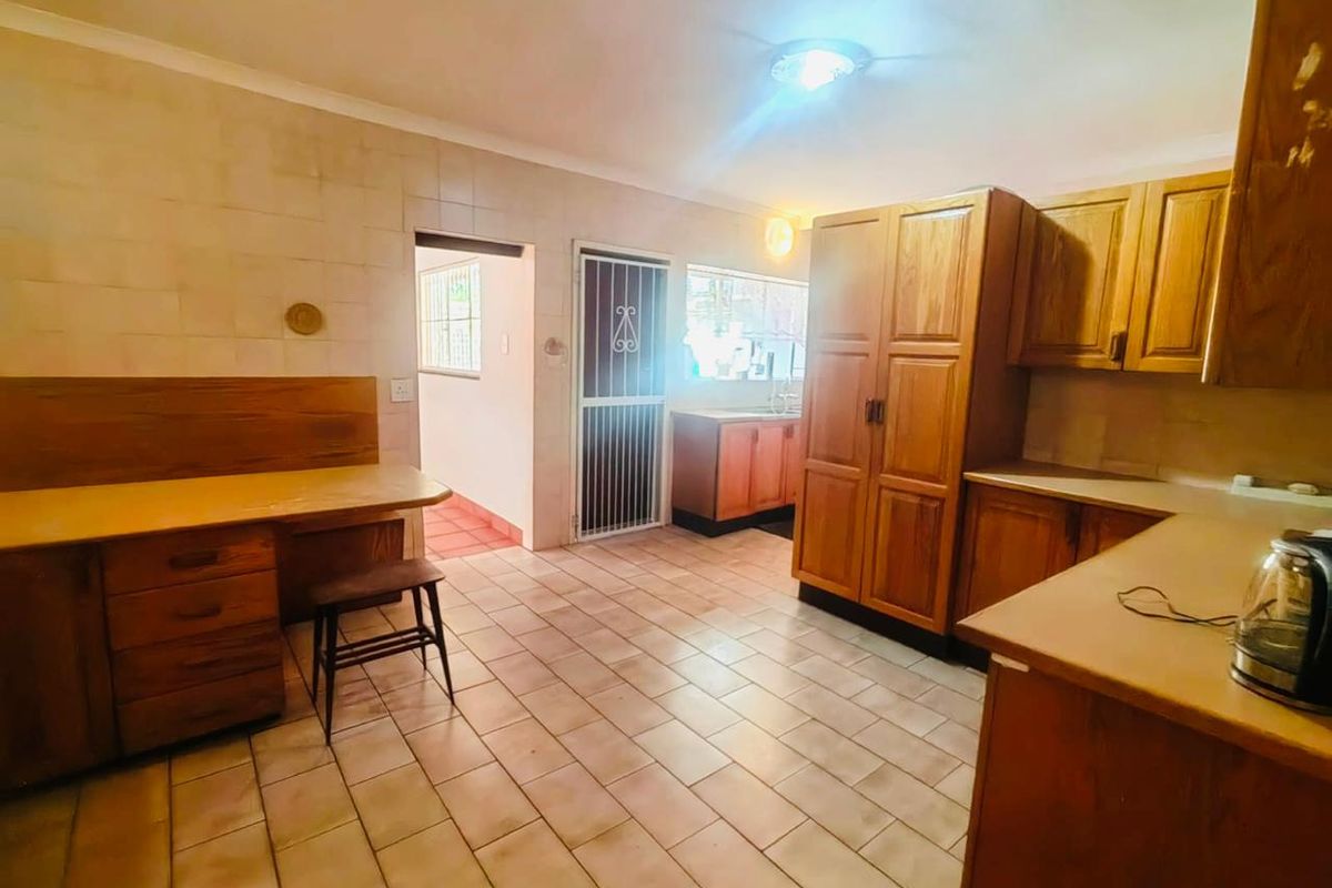 A functional kitchen featuring wooden cabinetry, tiled flooring, and a built-in desk area, offering a dated but practical layout with potential for modernization.