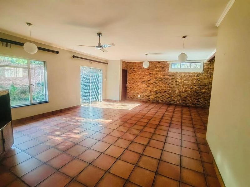 Spacious living area featuring terracotta floor tiles, an exposed brick feature wall, ceiling fan, and sliding glass doors leading to the exterior.