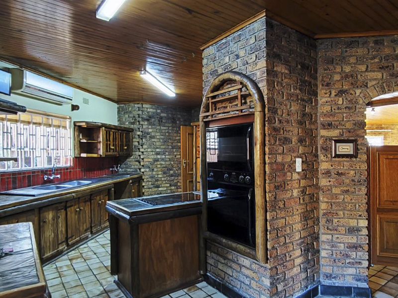 A rustic kitchen featuring exposed brick walls, timber ceiling, built-in oven, and ample wooden cabinetry with tiled flooring.