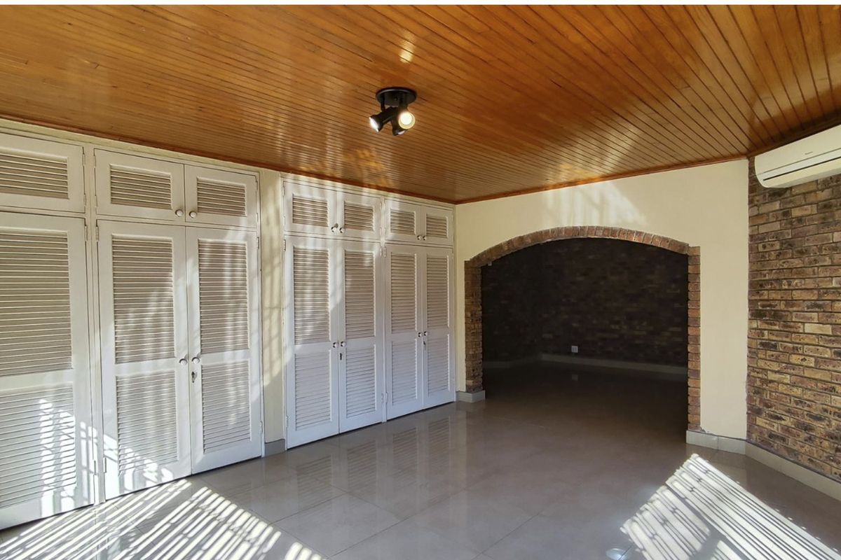 Spacious bedroom featuring extensive built-in cupboards, a warm timber ceiling, exposed brick accents, and a split-system air conditioner.
