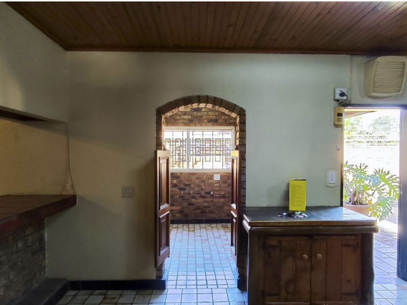 A rustic kitchen area featuring a timber ceiling, brick archway, and built-in brick counter, leading out to an exterior space.