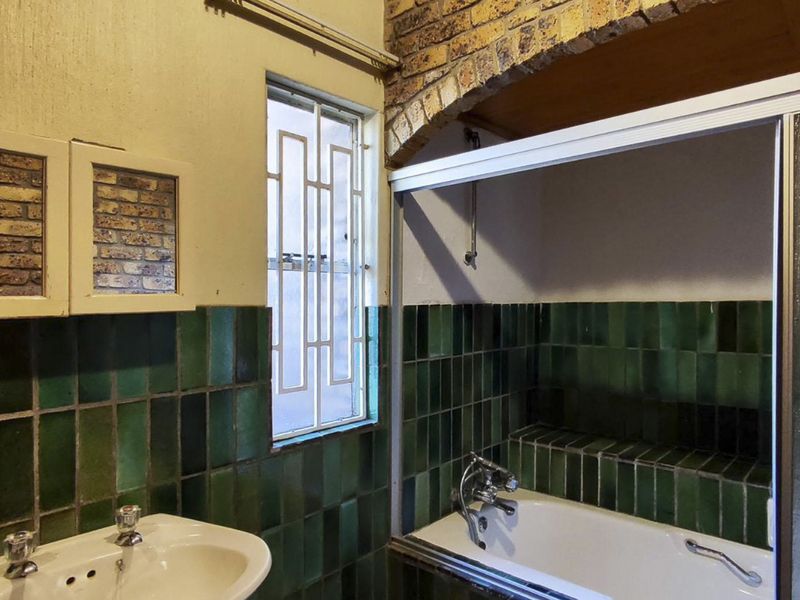 A dated bathroom featuring green wall tiles, a pedestal basin, and a shower-over-bath combination with a sliding glass screen.