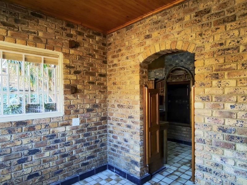 An empty living area featuring rustic exposed brick walls, a warm timber ceiling, and tiled flooring, with an arched doorway leading to an adjacent space.