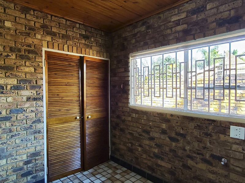 A functional laundry area featuring exposed brick walls, timber ceiling, tiled flooring, and built-in storage with louvered timber doors.