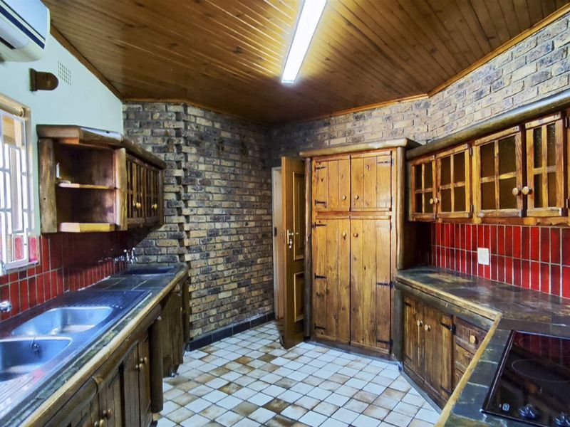 A rustic kitchen featuring exposed brick walls, wooden cabinetry, tiled countertops, and a double basin sink, offering a traditional aesthetic with functional layout.