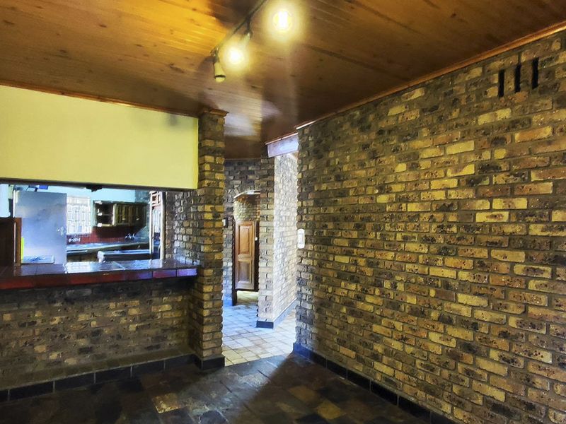 Open plan living area featuring rustic exposed brick walls, timber ceiling, and a breakfast bar counter connecting to the kitchen space.