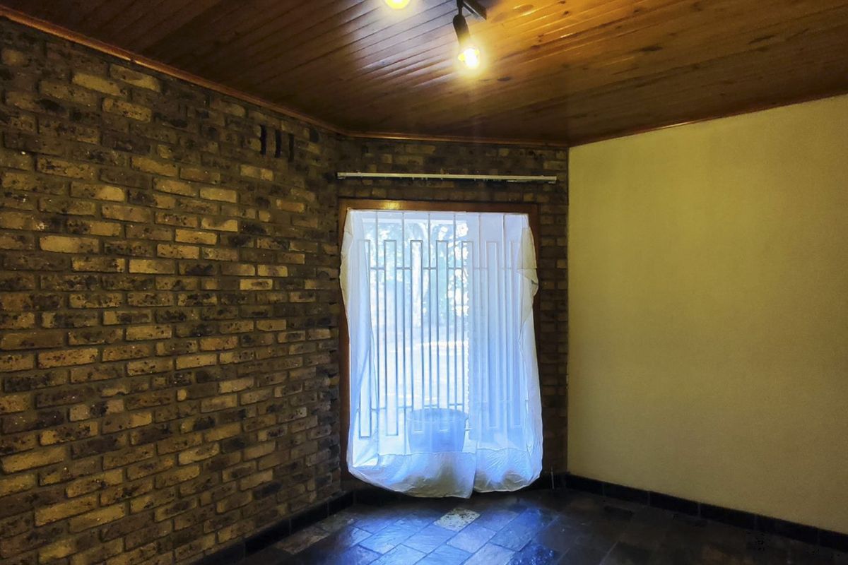 An empty living room featuring an exposed brick feature wall, timber ceiling, and tiled flooring, offering a blank canvas for renovation.