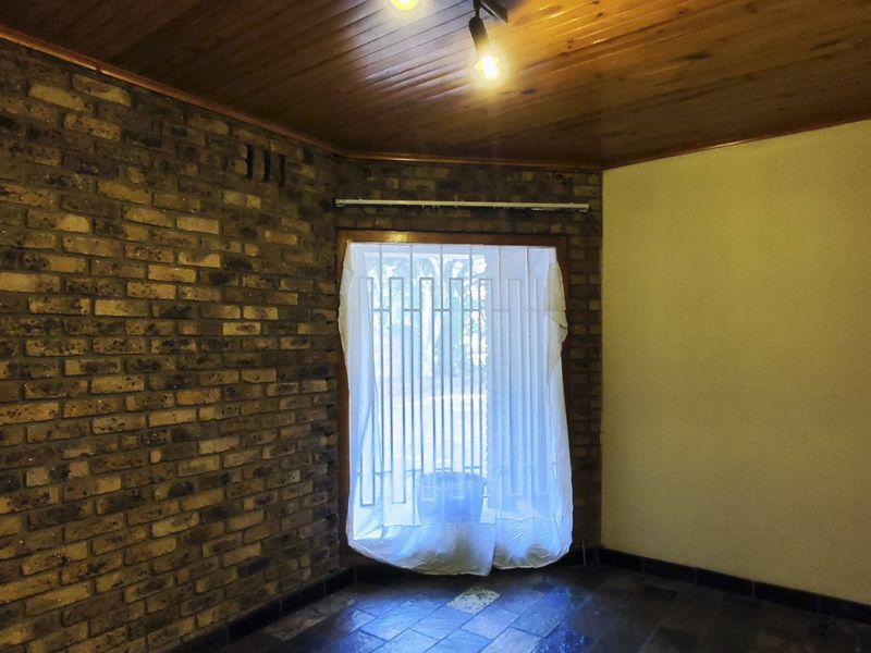 An empty living room featuring an exposed brick feature wall, timber ceiling, and tiled flooring, offering a blank canvas for renovation.