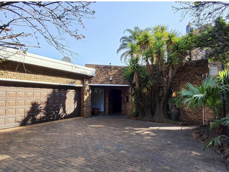 Front elevation of a face brick house featuring a paved driveway, double garage, and established garden entrance.