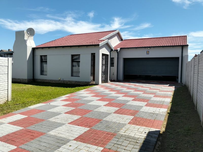 A well-maintained single-story house featuring a red tiled roof, a patterned paved driveway, and an integrated garage with a secure roller door.