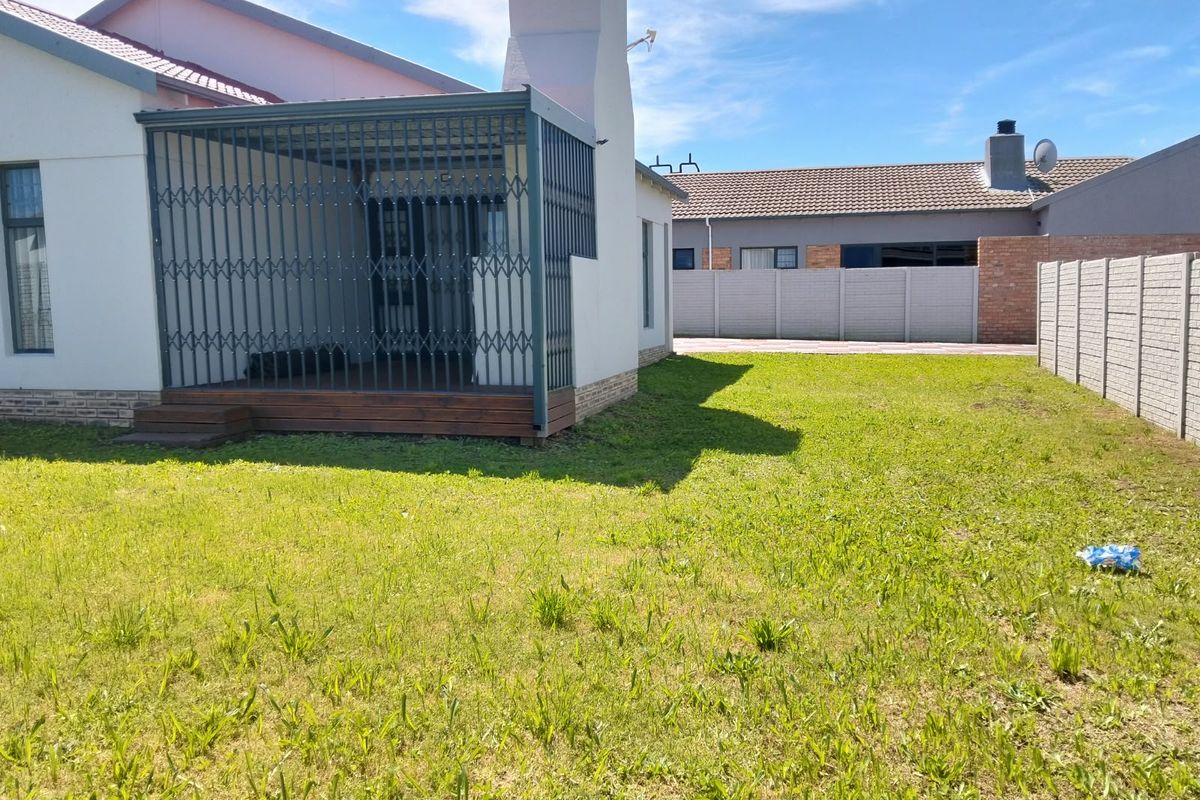 Rear view of the property featuring a covered patio with timber decking, a security gate, and a spacious private garden with boundary walling.