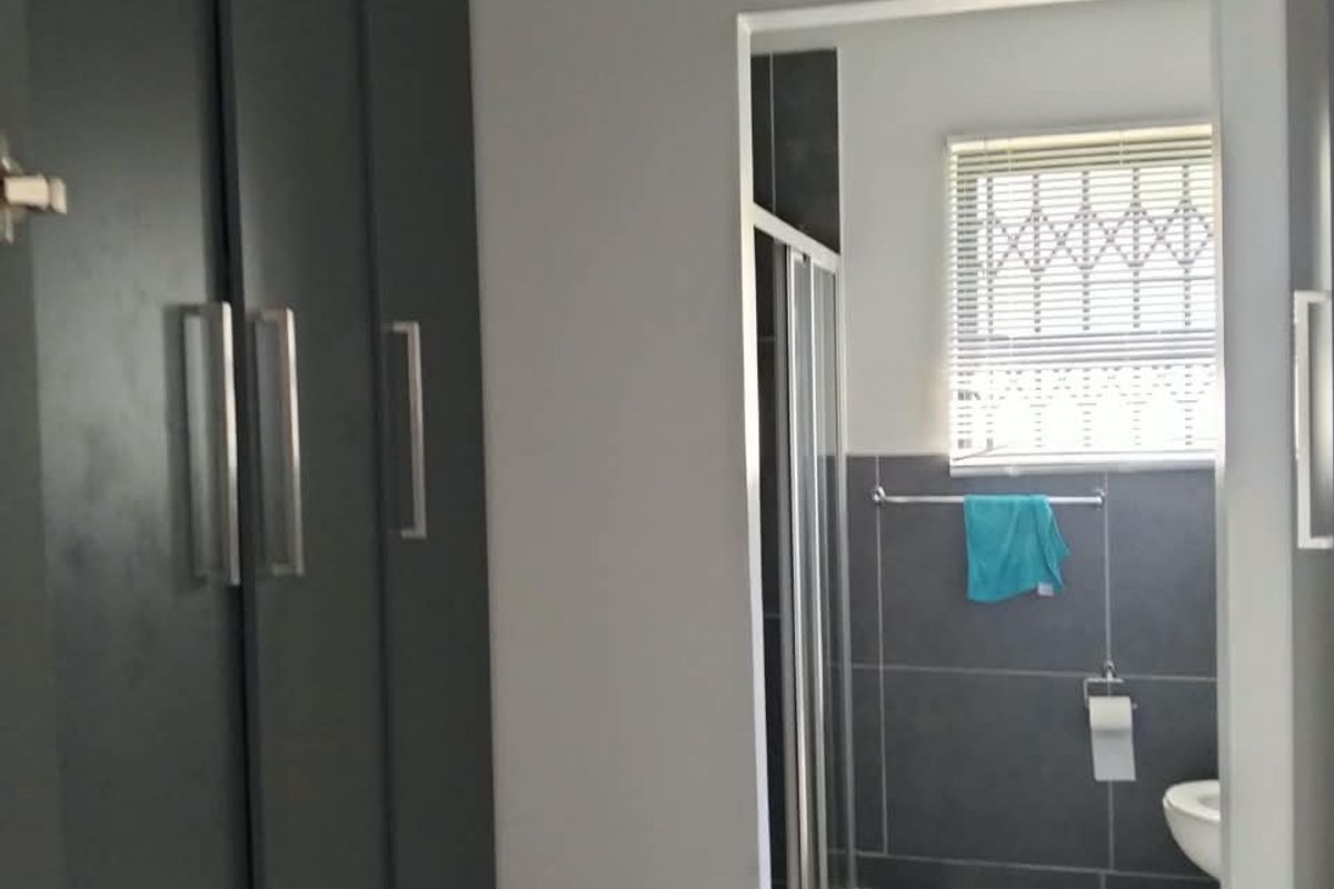 A modern bathroom featuring dark grey floor and wall tiles, built-in storage cupboards, a shower enclosure, and a toilet.