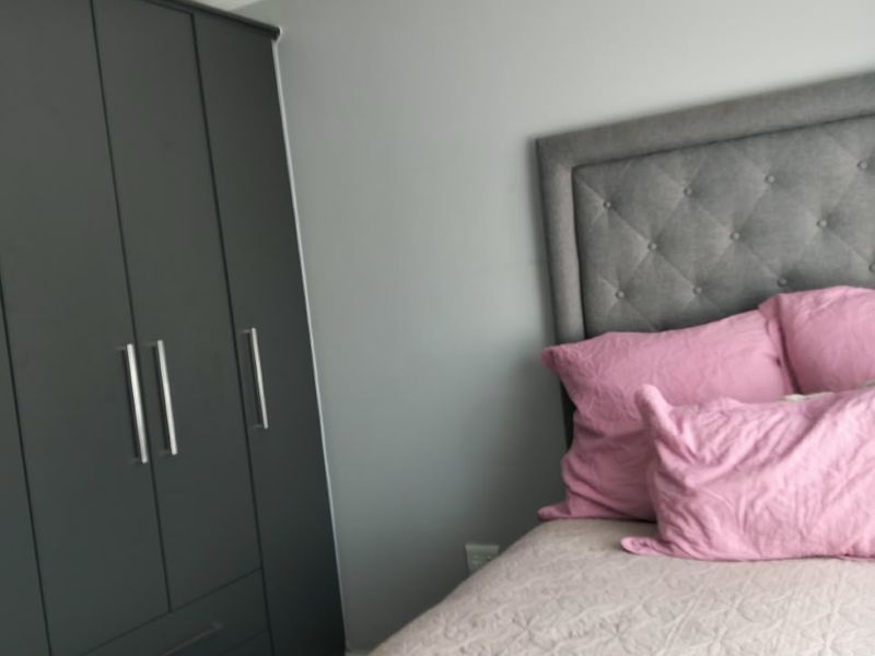A well-maintained bedroom featuring a modern dark grey built-in wardrobe, neutral wall finishes, and recessed ceiling lighting.