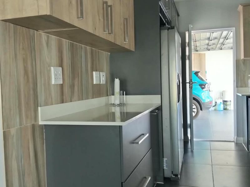 Modern kitchen featuring two-tone cabinetry, stone countertops, wood-look tiled splashback, and dark floor tiles, leading directly to the garage area.