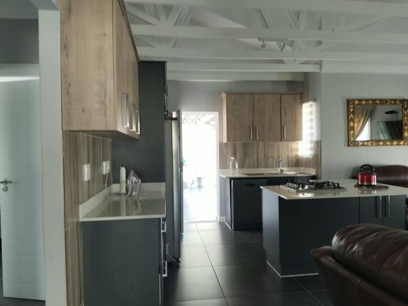 Modern open-plan kitchen featuring sleek cabinetry, stone countertops, a central island with a gas hob, and exposed ceiling beams.